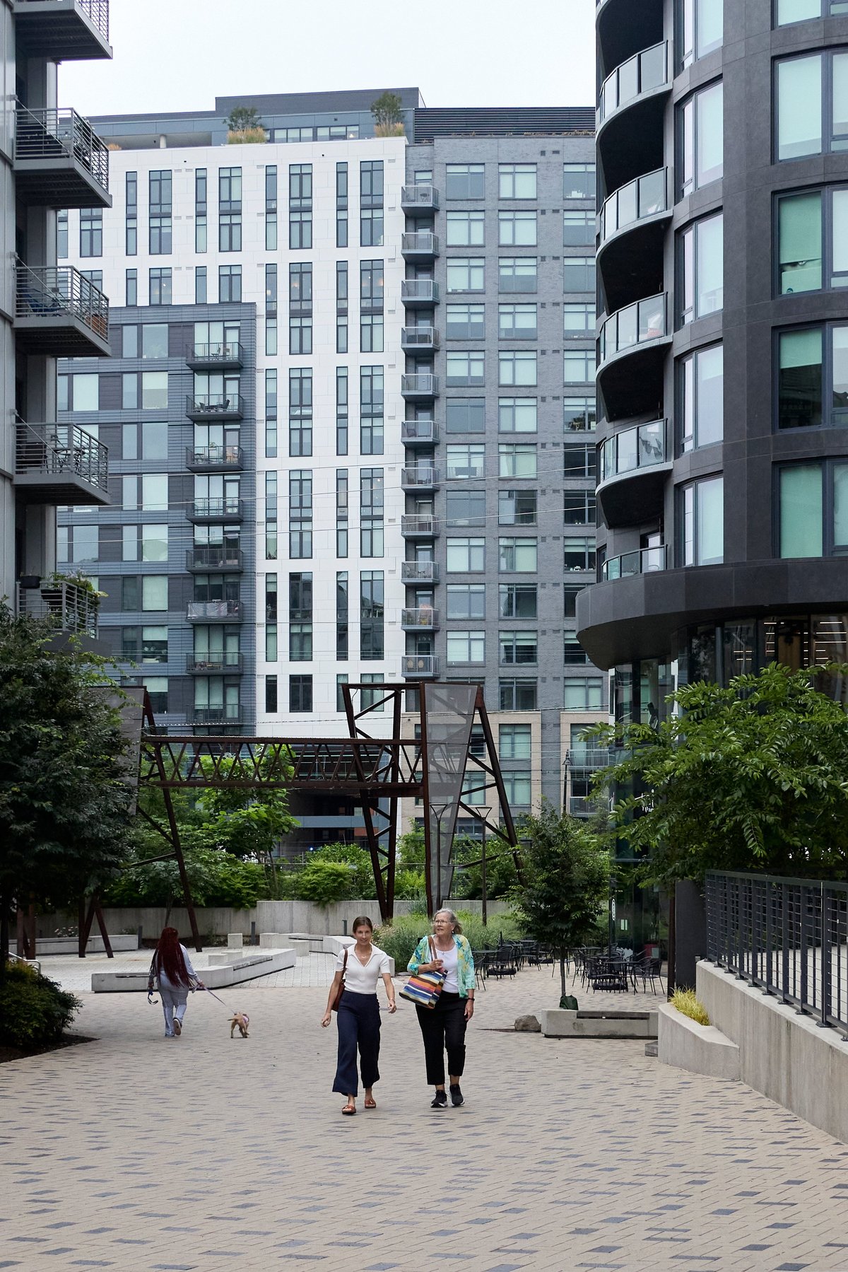 A new-build courtyard frames a patch of lawn where people pass apartment buildings and a dog trots along.